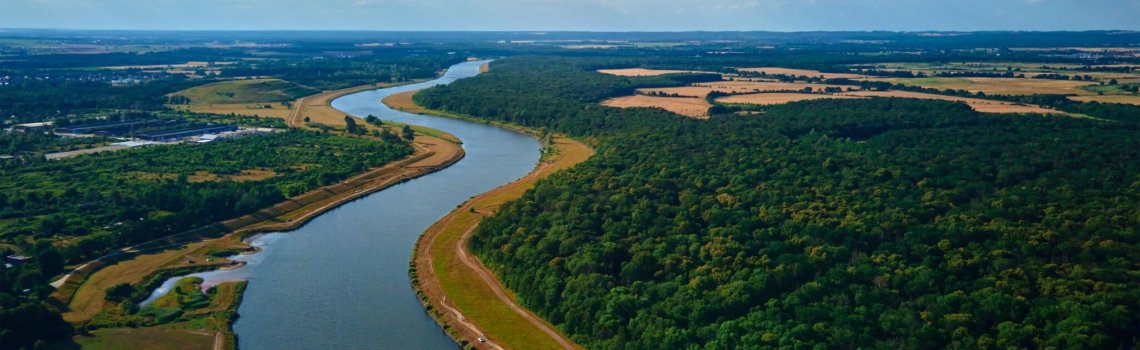 Aerial view of beautiful landscape with river winding through lush green forest and fields under bright blue sky with fluffy clouds